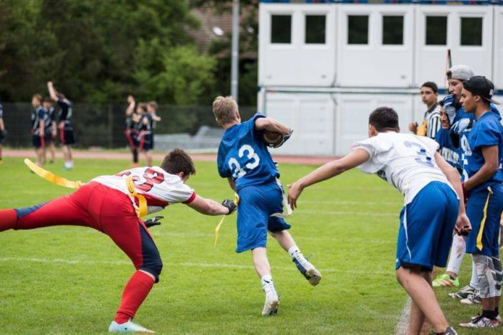 Flag football player is running, the defender trying to jump and catch the flag.